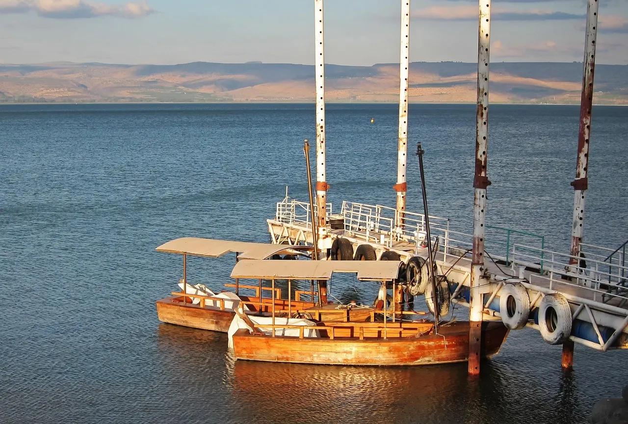 Bote de madera tradicional en el Mar de Galilea con agua tranquila y colinas verdes al fondo